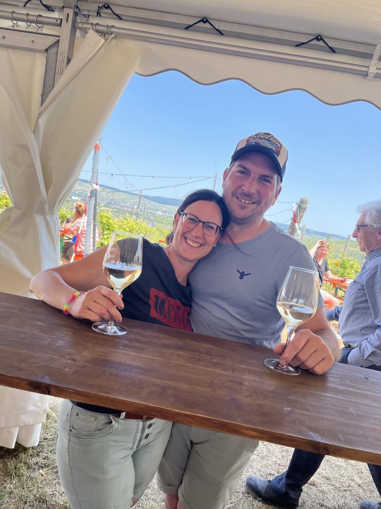 Jochen und Sabrina Eißele mit einem Glas Eißele Wein auf den Weinfeldern des Familienweinguts